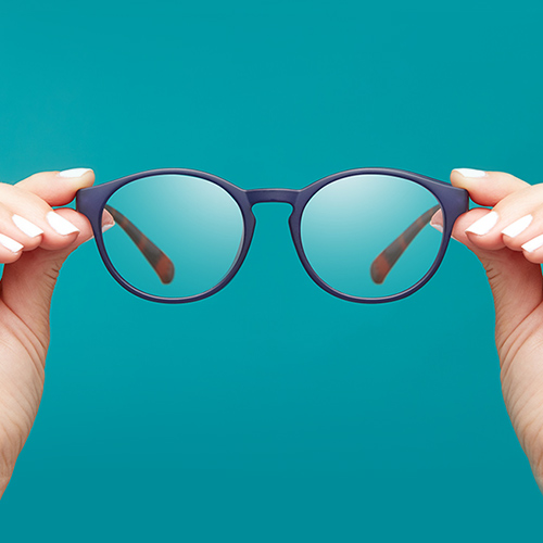 Blue-framed round eyeglasses held by hands with white nail polish against a turquoise background.