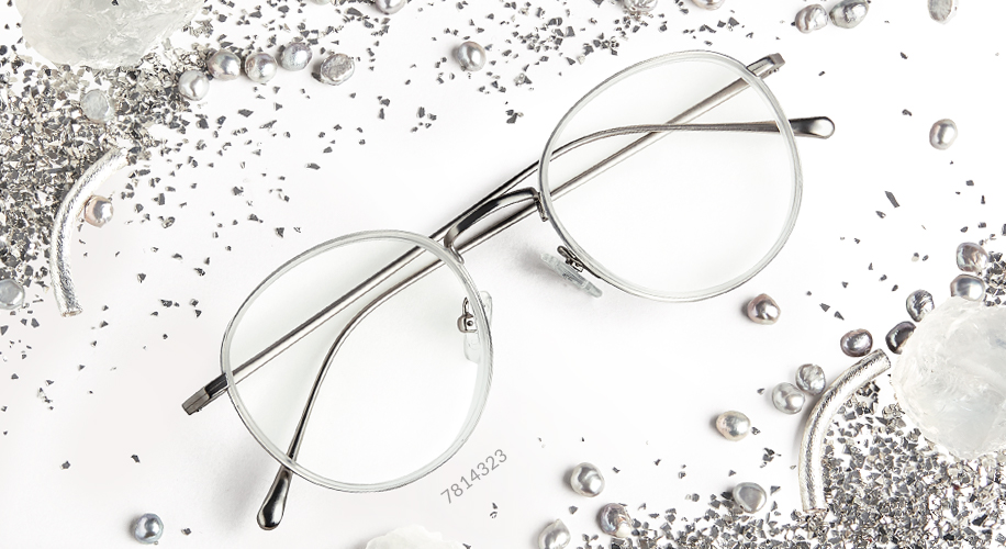 Round metal eyeglasses with thin silver frames and number 7814323. Surrounded by decorative silver glitter and beads.