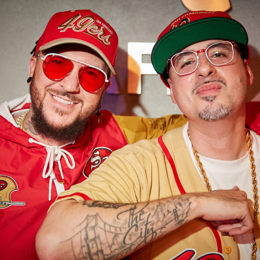 Two men wearing San Francisco 49ers caps and jerseys. Tattoo on one arm says, "The City".