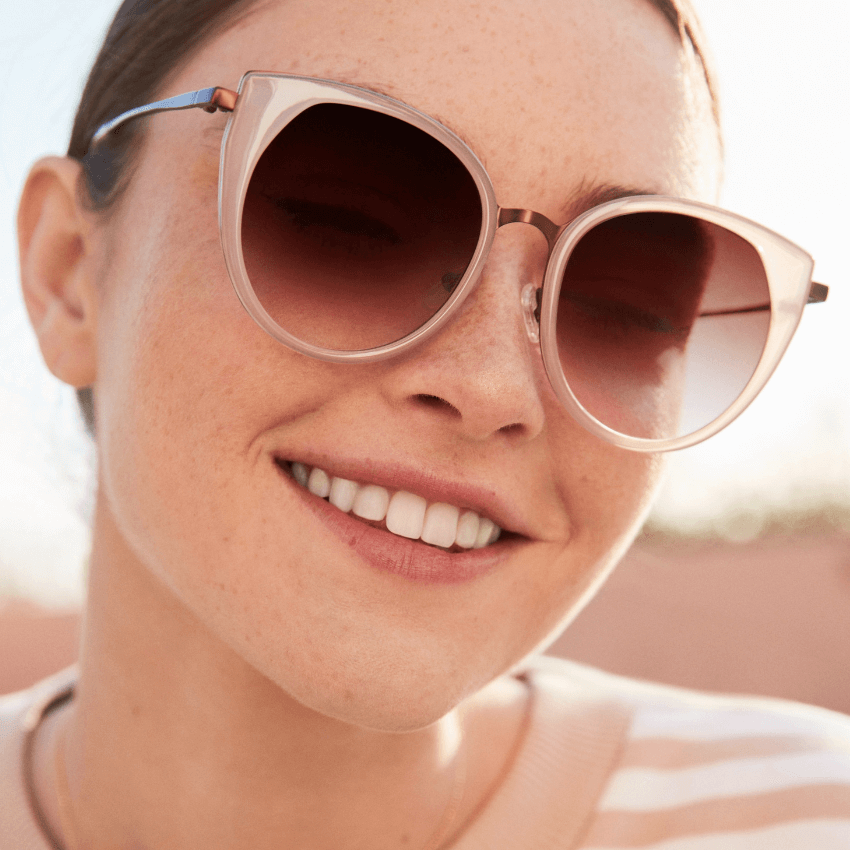 Woman wearing round, pink gradient lens sunglasses with transparent, light pink frames.