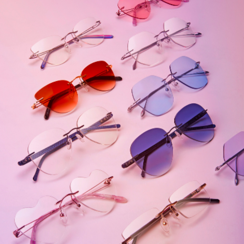 Colorful sunglasses with various lens shapes, including heart, aviator, and square, on a pink gradient background.
