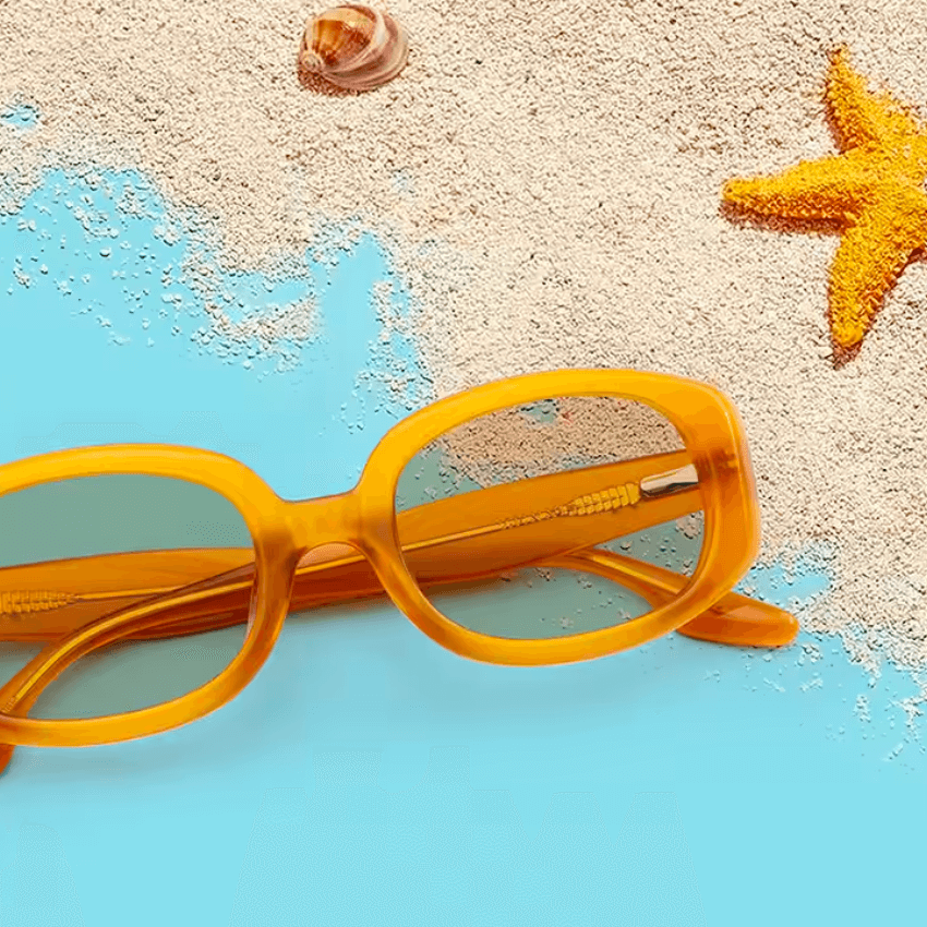 Yellow-framed sunglasses on blue surface with sand, seashell, and starfish