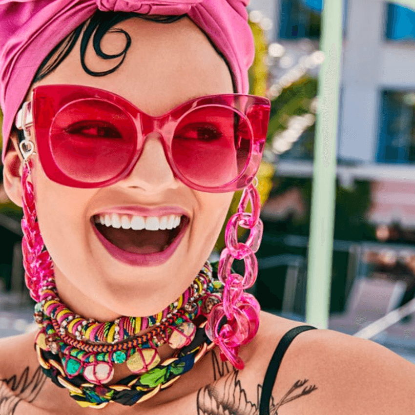 Woman wearing oversized pink sunglasses with heart-shaped accents and a colorful beaded necklace.