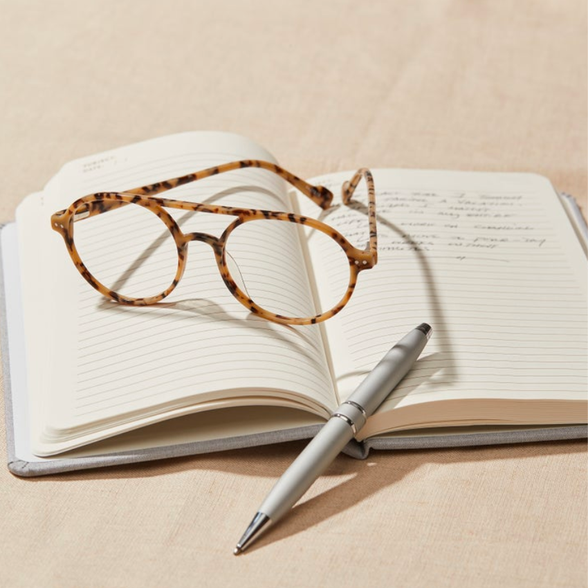 Tortoiseshell eyeglasses and silver pen resting on an open lined notebook.
