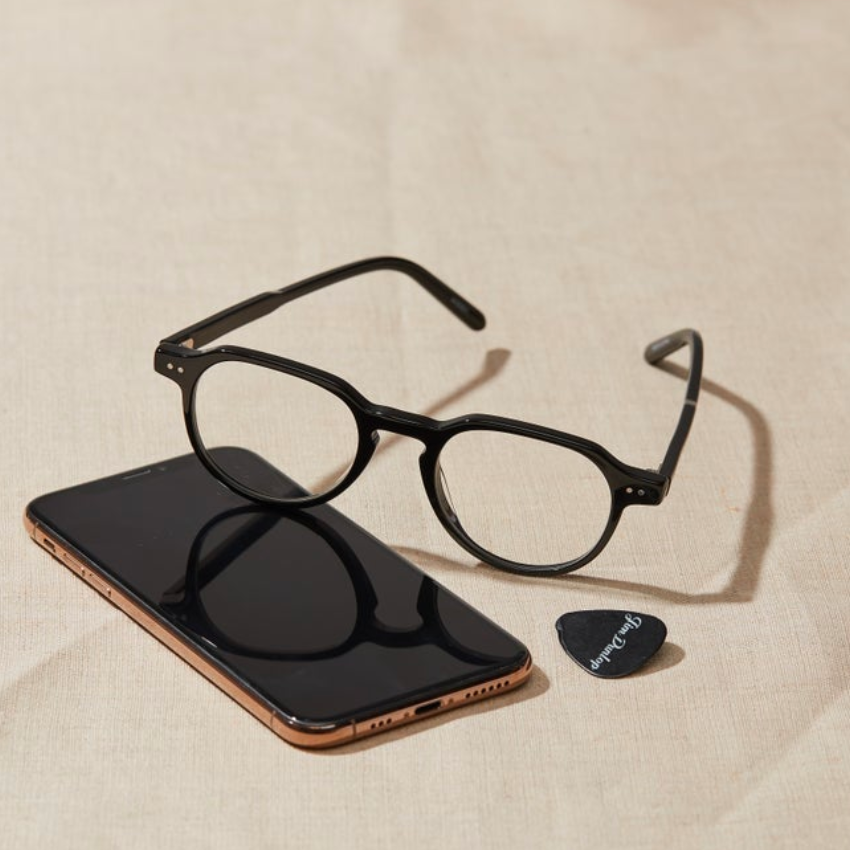 Black eyeglasses, smartphone, and guitar pick with text "Fender" on a light-colored surface.