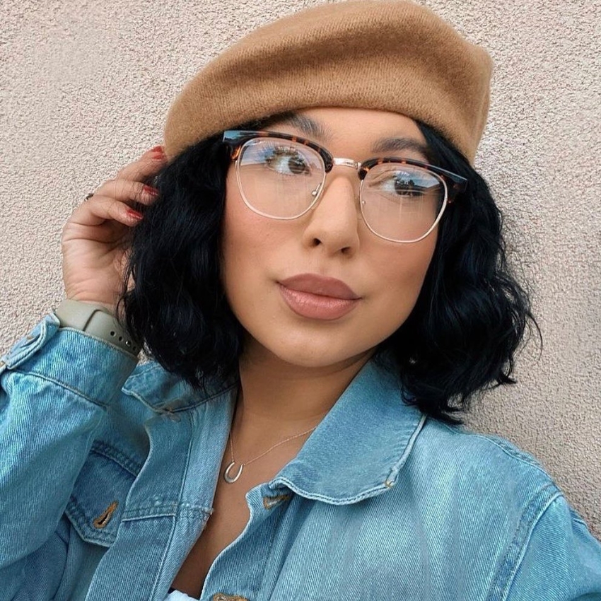 Woman wearing tortoiseshell glasses, camel-colored beret, denim jacket, silver necklace, and green smartwatch.