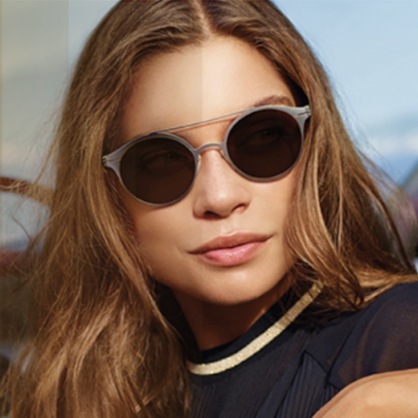 Woman wearing round, dark-tinted sunglasses with clear and silver frames.