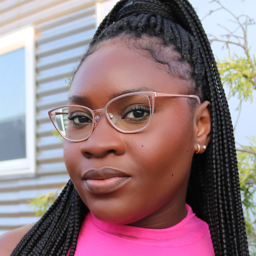 Woman wearing clear pink-framed glasses, braided hair styled in a high ponytail, and a pink top.