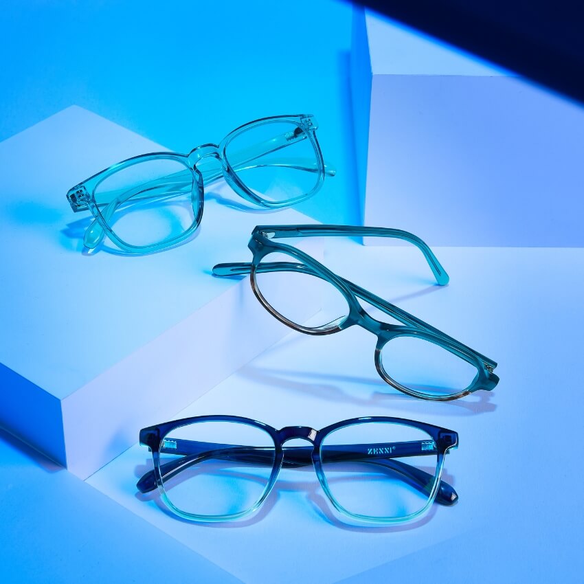 Three pairs of eyeglasses with clear, translucent, and dark frames are displayed against a blue background.