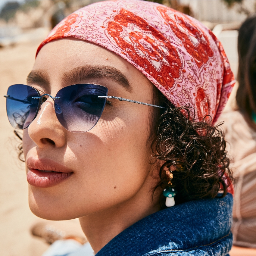 Person wearing sunglasses with blue-gray gradient lenses and a pink and red patterned headscarf.