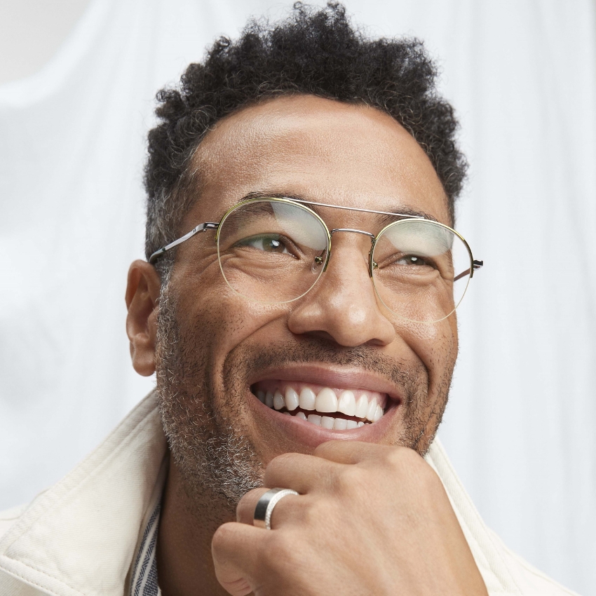 Man wearing round metal frame glasses and a silver band ring on his finger, smiling widely.