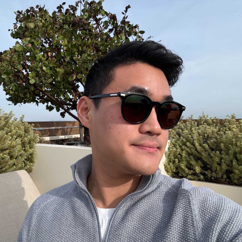 Man wearing black sunglasses and a light gray zip-up sweater outdoors.