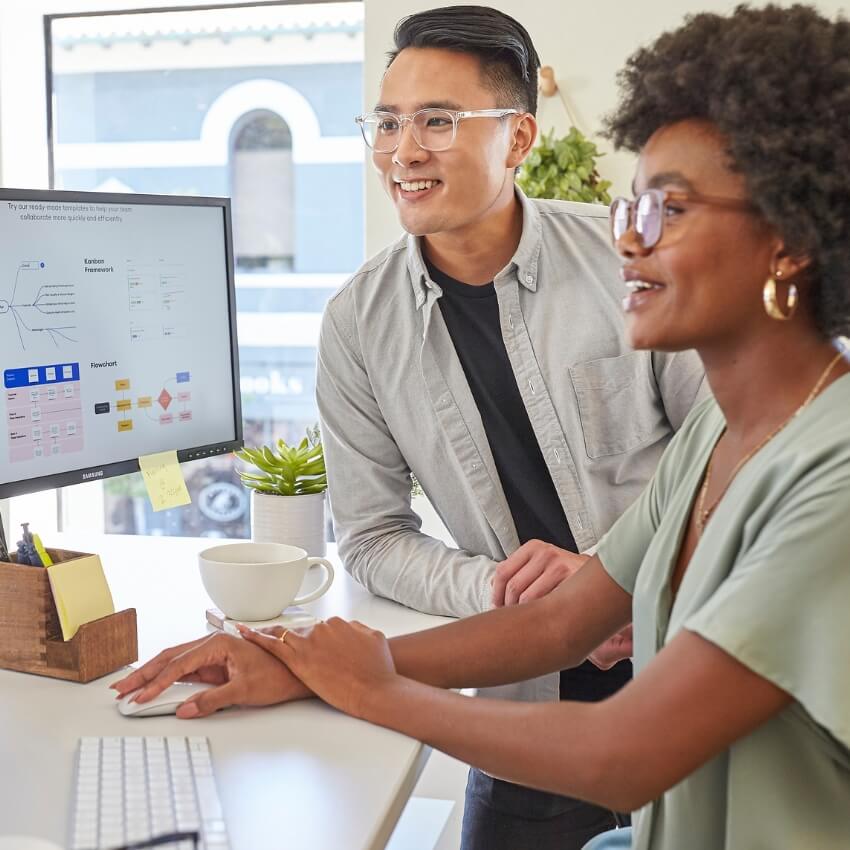 Two colleagues collaborating at a desk with a Samsung monitor displaying a flowchart.