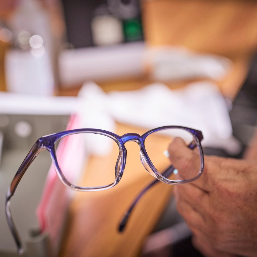 Blue and clear eyeglasses held by a person's hand.