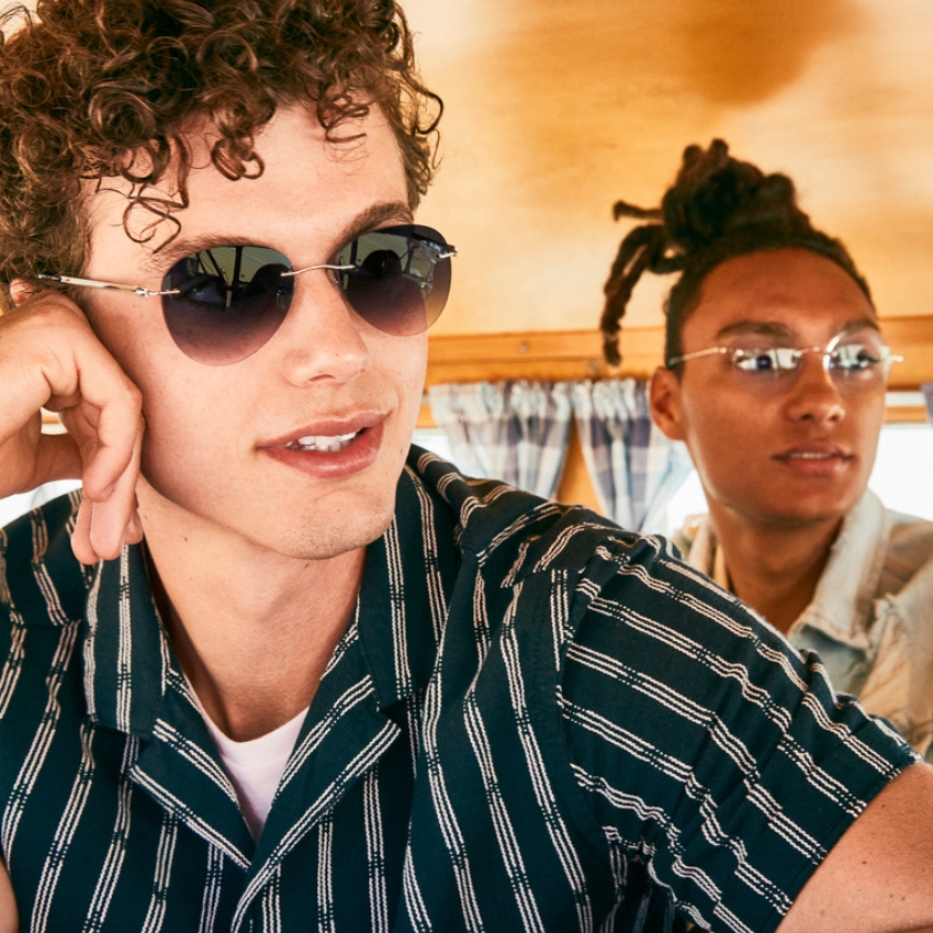 Man in sunglasses and striped shirt, another person in the background wearing glasses and a denim jacket.