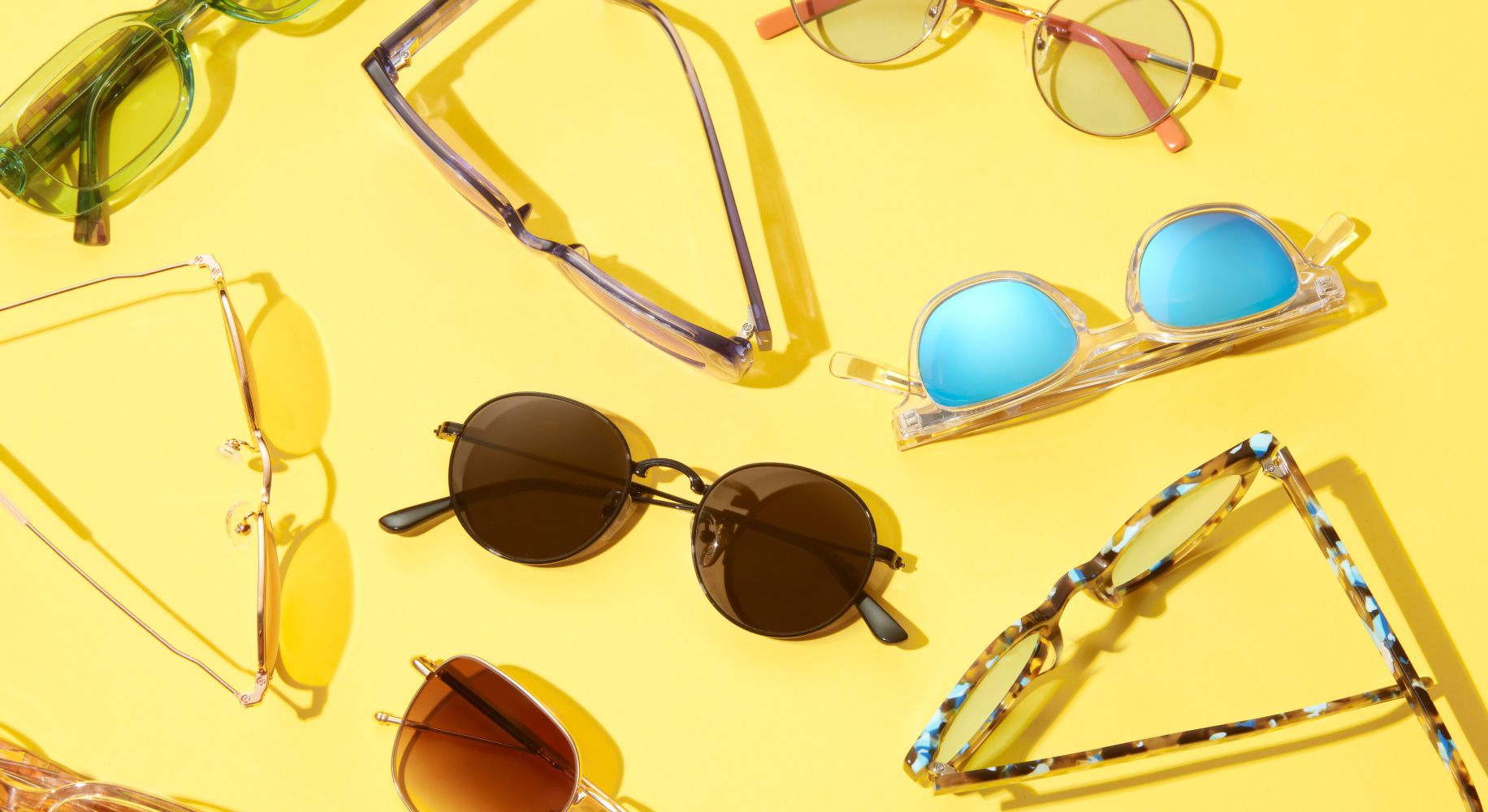 Various styles of sunglasses and eyeglasses arranged on a bright yellow background.