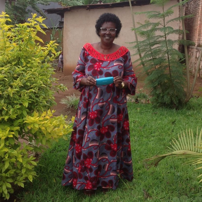 Woman wearing a long, colorful dress with red patterns and holding a blue item in a garden.