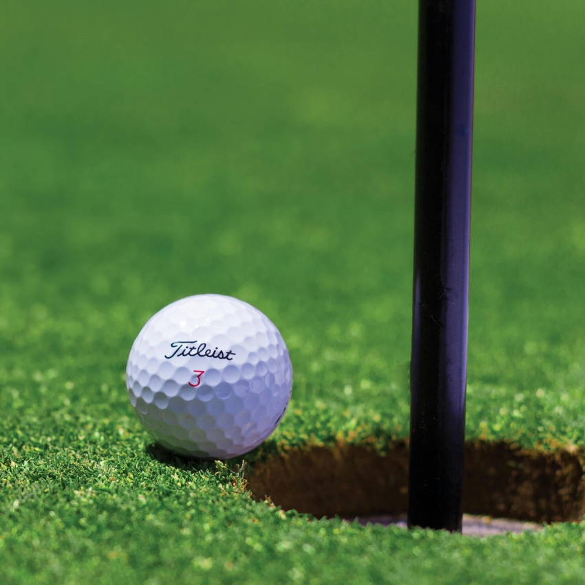 Titleist golf ball next to the hole on a green. The ball features the logo in black and the number 3 in red.