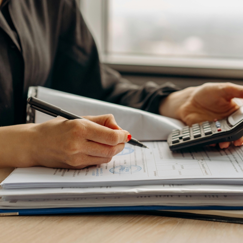 Hand holding a pen filling out documents while other hand uses a calculator.