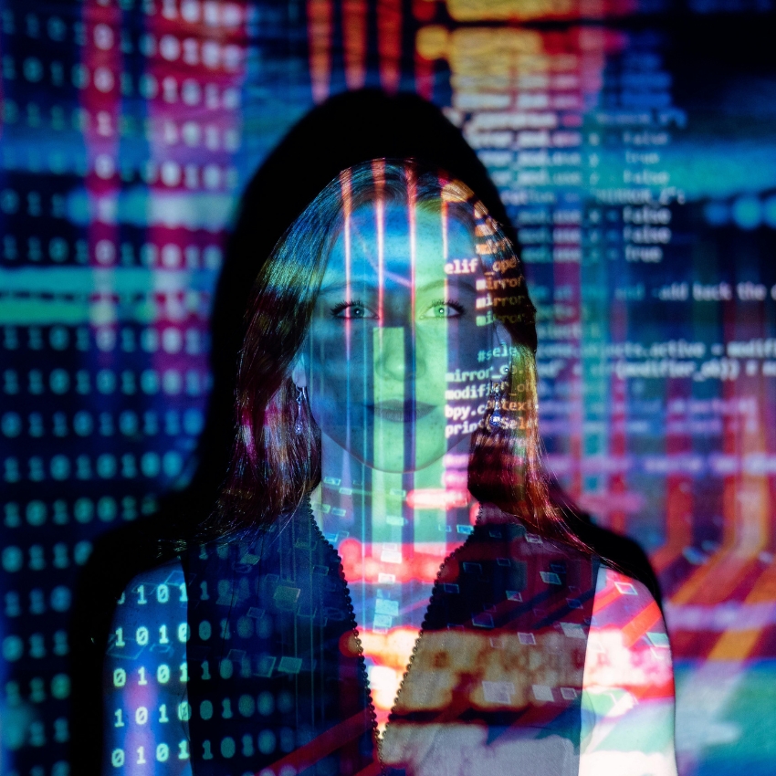 Colorful code projections on a woman’s face with lines of programming code and binary digits.